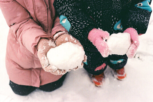 Siblings holding snowballs in a winter park.