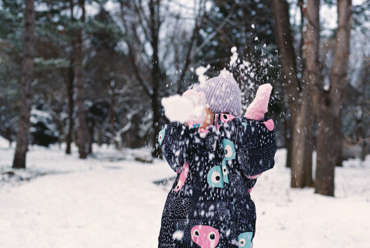 A little girl dodges a snowball while playing in a winter park.