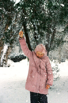 A teenager girl pulling on a branch with snow in a winter park.