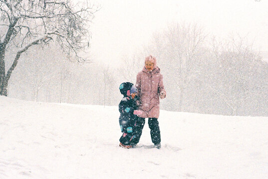 Siblings having fun while snowfall in a winter park.