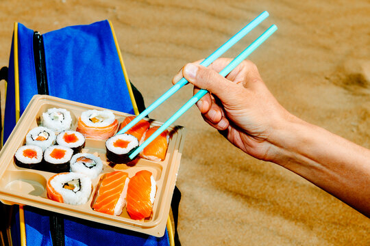 a man grabs a maki roll with blue chopsticks from a tray
