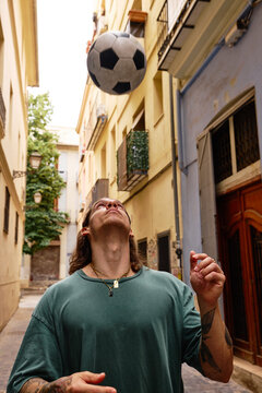 Man juggling a football ball in a narrow street in a city