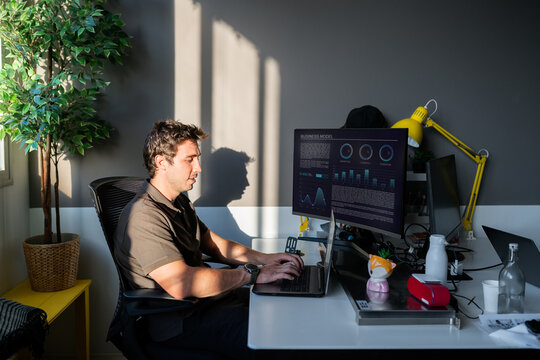 Man working on laptop and monitors in office