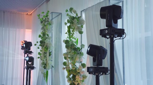 Festive atmosphere and lighting equipment at the party. Spotlights in the banquet hall near a flower-decorated wedding arch. Disco lighting. Moving white beams on stands during disco at party.