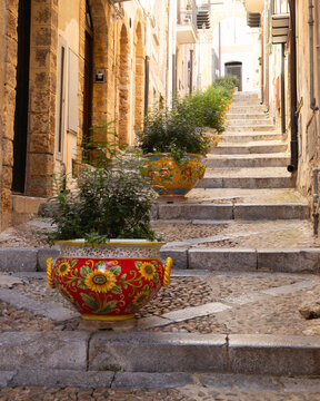 Charming Italian alleyway with decorative planters and stone steps in Cefalu, Sicily, Italy.