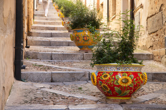 Charming Italian alleyway with decorative planters and stone steps in Cefalu, Sicily, Italy.