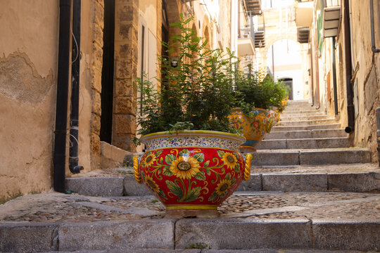 Charming Italian alleyway with decorative planters and stone steps in Cefalu, Sicily, Italy.
