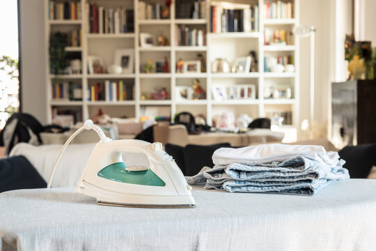 Modern iron on ironing board with clothes at home.