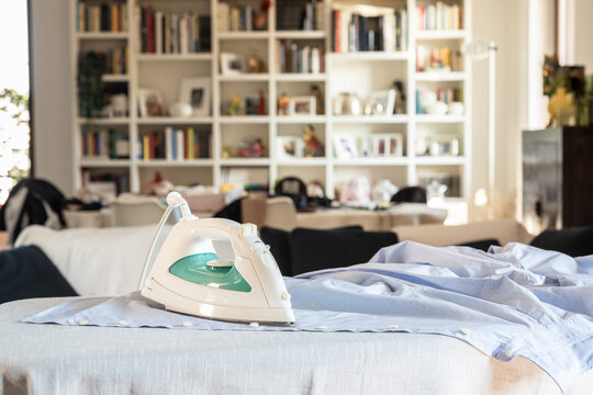Modern electric iron on a shirt on ironing board at home.