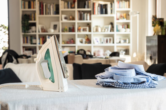 Modern iron on ironing board with clothes at home.