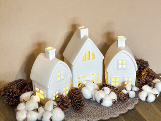 Glowing ceramic village houses styled with cotton bolls and pinecones in a neutral palette, creating a cozy Scandinavian scene for autumn, winter, Thanksgiving and Christmas. © Ryan