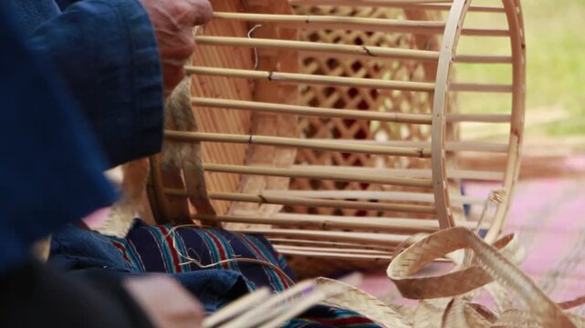 Close-up of an elderly Thai artisan skillfully weaving a handmade bamboo basket using traditional techniques in a rural village of Northern Thailand. The image highlights sustainable craftsmanship, na