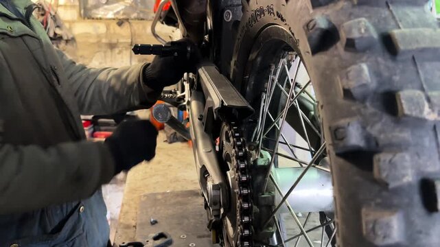 Professional mechanic repairing detail of motorcycle at workplace. Male repairer fixing moto at workshop. Adult repairman mending vehicle at garage. Concept of maintenance service. Slow motion