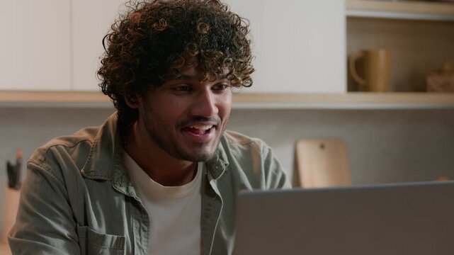 Happy Indian freelancer business man celebrating win laptop at home kitchen shocked Arabian male businessman guy reading good news online victory achievement success computer betting service result