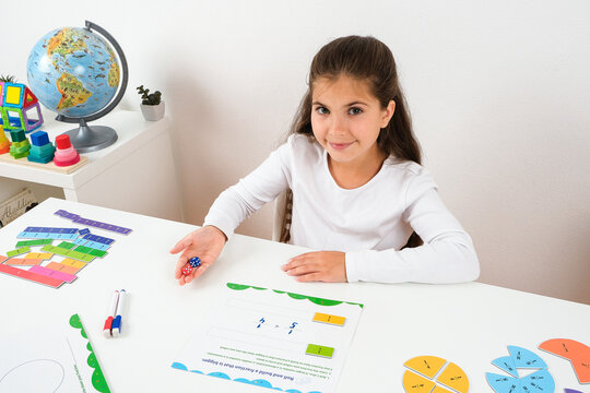 Focused little girl studying math fractions with magnetic circles at her desk for homeschooling