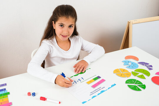 Focused little girl studying math fractions with magnetic circles at her desk for homeschooling