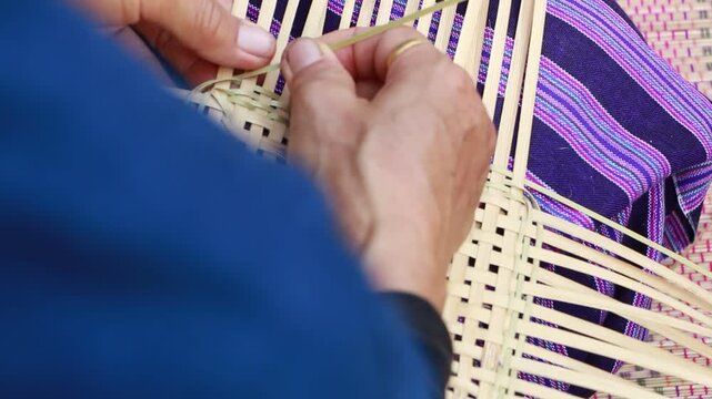 Close-up of an elderly Thai artisan skillfully weaving a handmade bamboo basket using traditional techniques in a rural village of Northern Thailand. The image highlights sustainable craftsmanship, na