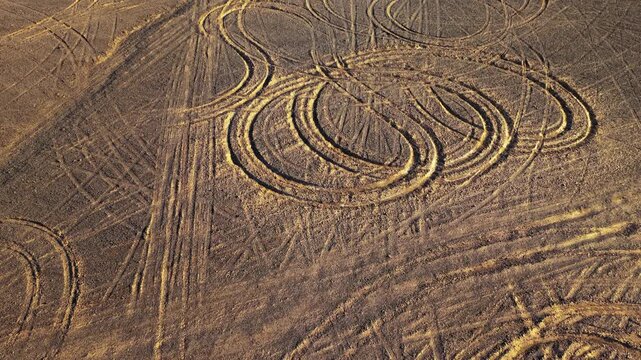 Aerial view of curved tire tracks embedded on dry dirt ground.