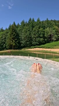 Female feet in a hot tub and whirlpool facing the woods. Vertical