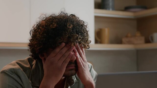 Stressed Indian freelancer man with headache using laptop at home kitchen Arabian male ethnic businessman suffering migraine muscle tension overwork business problem computer pain exhausted burnout