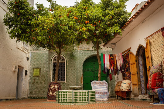 Traditional Moroccan courtyard with vibrant mosaic tiles, orange trees, handcrafted Berber rugs and souvenir shops in the heart of Chefchaouen, the famous Blue City in northern Morocco