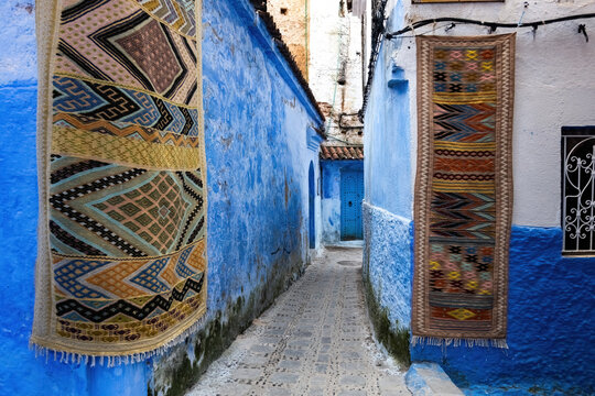 Narrow street decorated with traditional moroccan carpets in blue town of Chefchaouen in Morocco