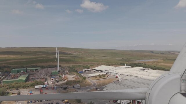 Cinematic drone footage flying between the rotating blades of a wind turbine at a wind farm in Wales. Close aerial pass showcasing renewable energy infrastructure, modern wind power technology and sus