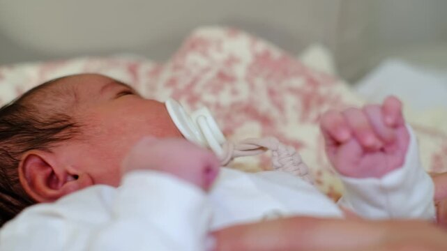 The camera lingers near a newborn face as a pacifier rests in the mouth and a caregiver hand moves gently nearby. This scene suits comfort, protection, early parenthood, and tender home care.