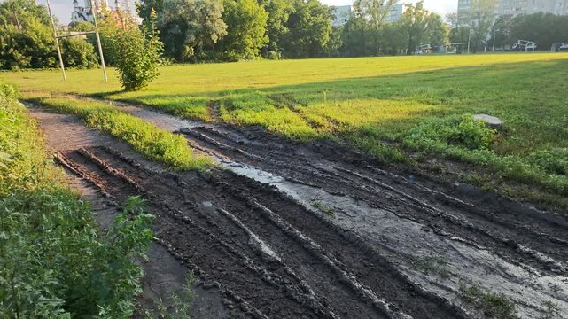 Panning view of deep heavy equipment tire tracks on a muddy dirt road along a green field.