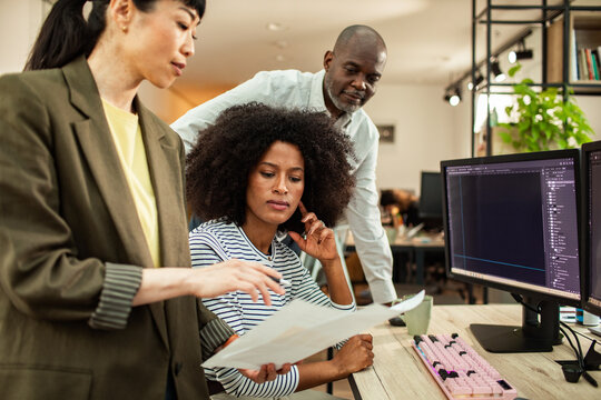 Diverse coworkers collaborating at computer in modern office