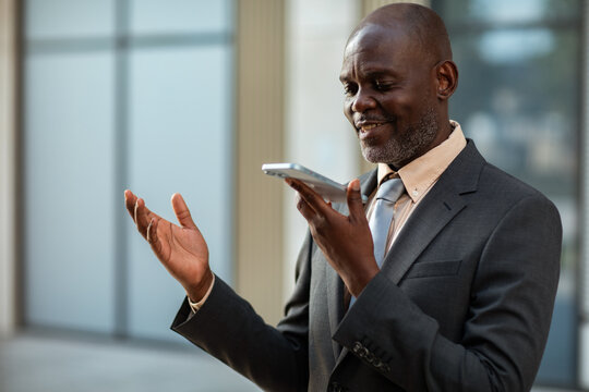 Senior businessman using voice assistant on smartphone in office lobby
