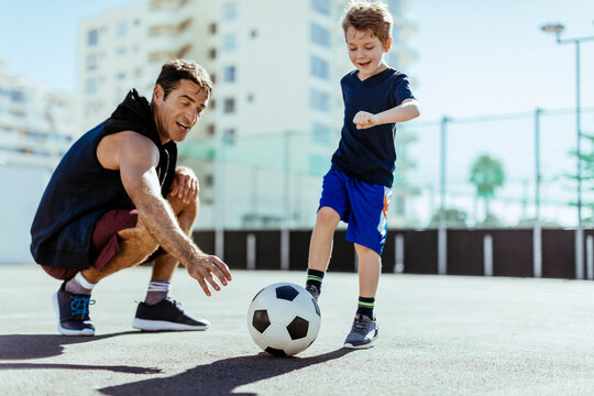 Man coaching boy playing soccer on outdoor court