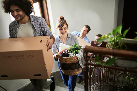Friends carrying boxes up apartment stairs while moving in