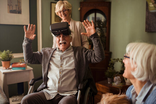 Senior man in wheelchair trying virtual reality at home with friends