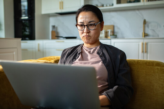 Concerned woman using laptop on couch in home kitchen