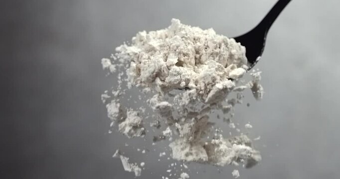Flour falling from black spoon in super slow motion