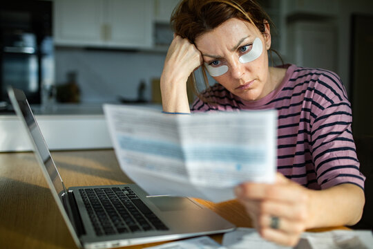 Woman with eye patches reviewing bills at kitchen table