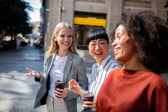 Three diverse women laughing with coffee on city street