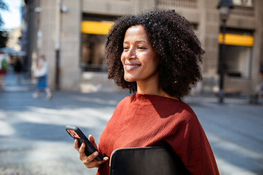Smiling woman with smartphone and laptop on sunny city street