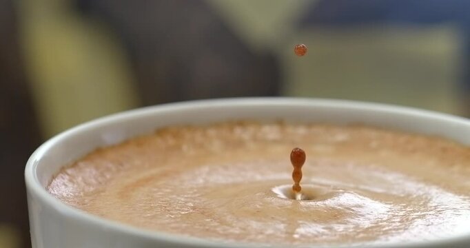 Coffee drop falling into cup creating a splash and ripple in crema super slow motion