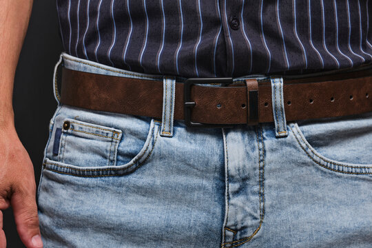 Close up shot man wearing light blue denim jeans with brown leather belt buckle.