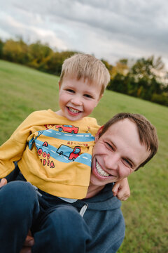 Dad carrying and hugging little boy outdoors in autumn field. Father and son smiling and having fun together during a walk in nature. Closeup.