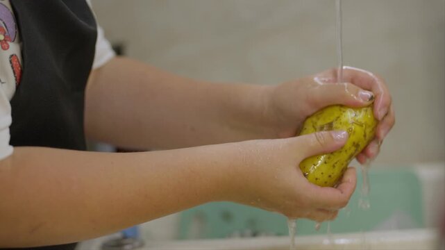 A woman in a black apron washes potatoes under running water