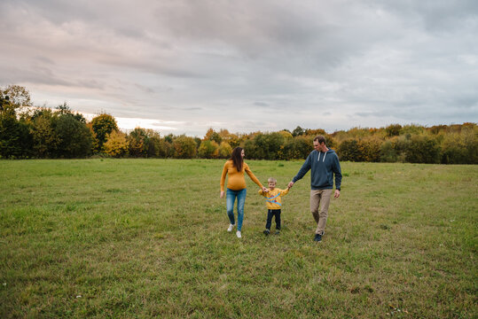 Mother, father and son walking together holding hands outdoors in autumn field. Family having a walk in nature.