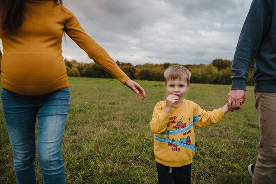 Close up view on hands holding hands, mother, father and son outdoors in autumn field. Family walking together in nature.