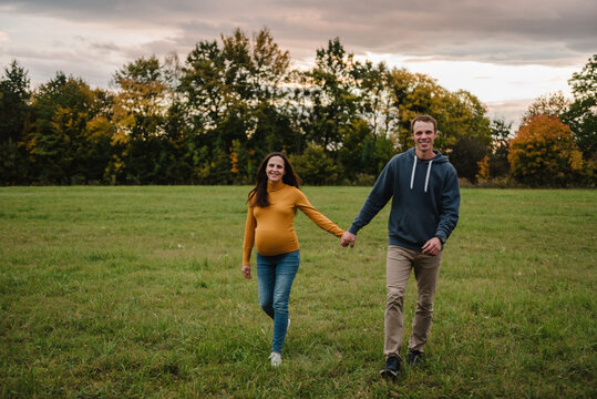 Woman and man holding hands and walking together in nature in field in autumn weather. Pregnant female and male having a walk outdoors.