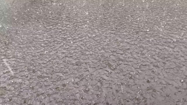 Close up of raindrops hitting wet asphalt, creating ripples and water splashes during heavy rain. Atmospheric urban weather background with natural rainfall and textured pavement surface.