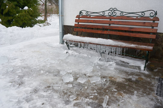 Wooden garden bench with long icicles hanging from the frozen seat, Frozen wooden bench covered with snow and ice in the backyard in winte