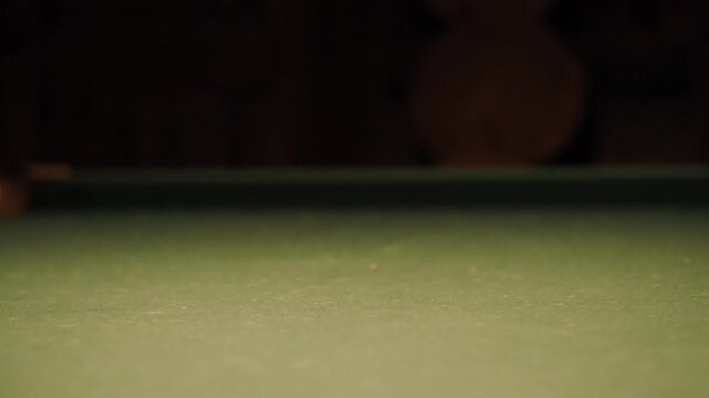 Close up view of a green felt pool table. A striped 14 ball sits in the foreground. A white cue ball strikes the 14 ball. Both balls roll across the surface and exit the frame. Static low angle