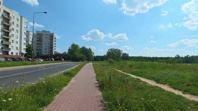 Paved sidewalk leading from apartment blocks into green field path